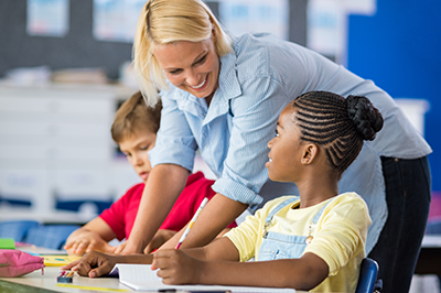 smiling teacher assisting students at desk